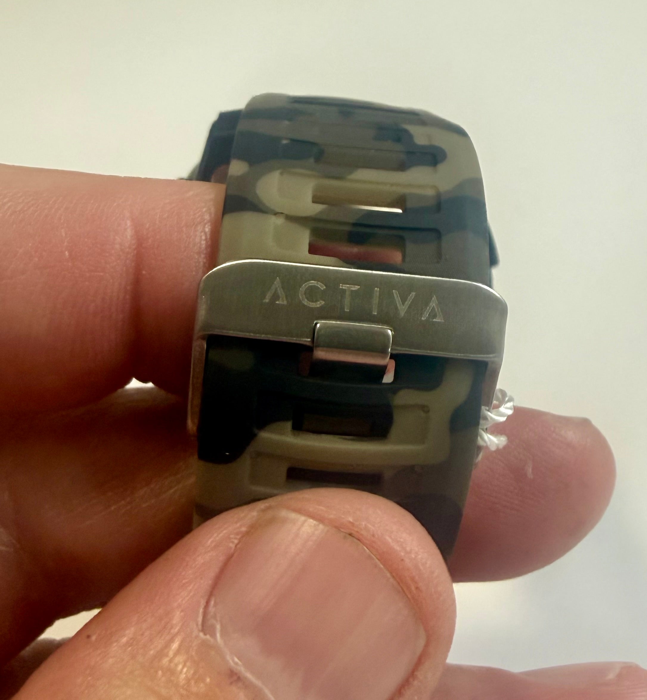 Camouflage watch band with 'Activa' clasp held between fingers against a white background