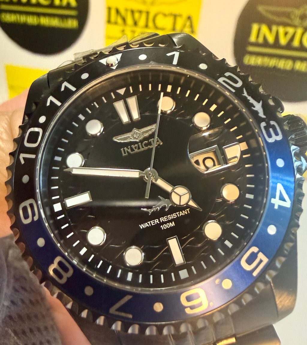 Invicta Mens Pro Diver Black and blue  watch with black dial and blue bezel held in a hand, with brand logos in the background.