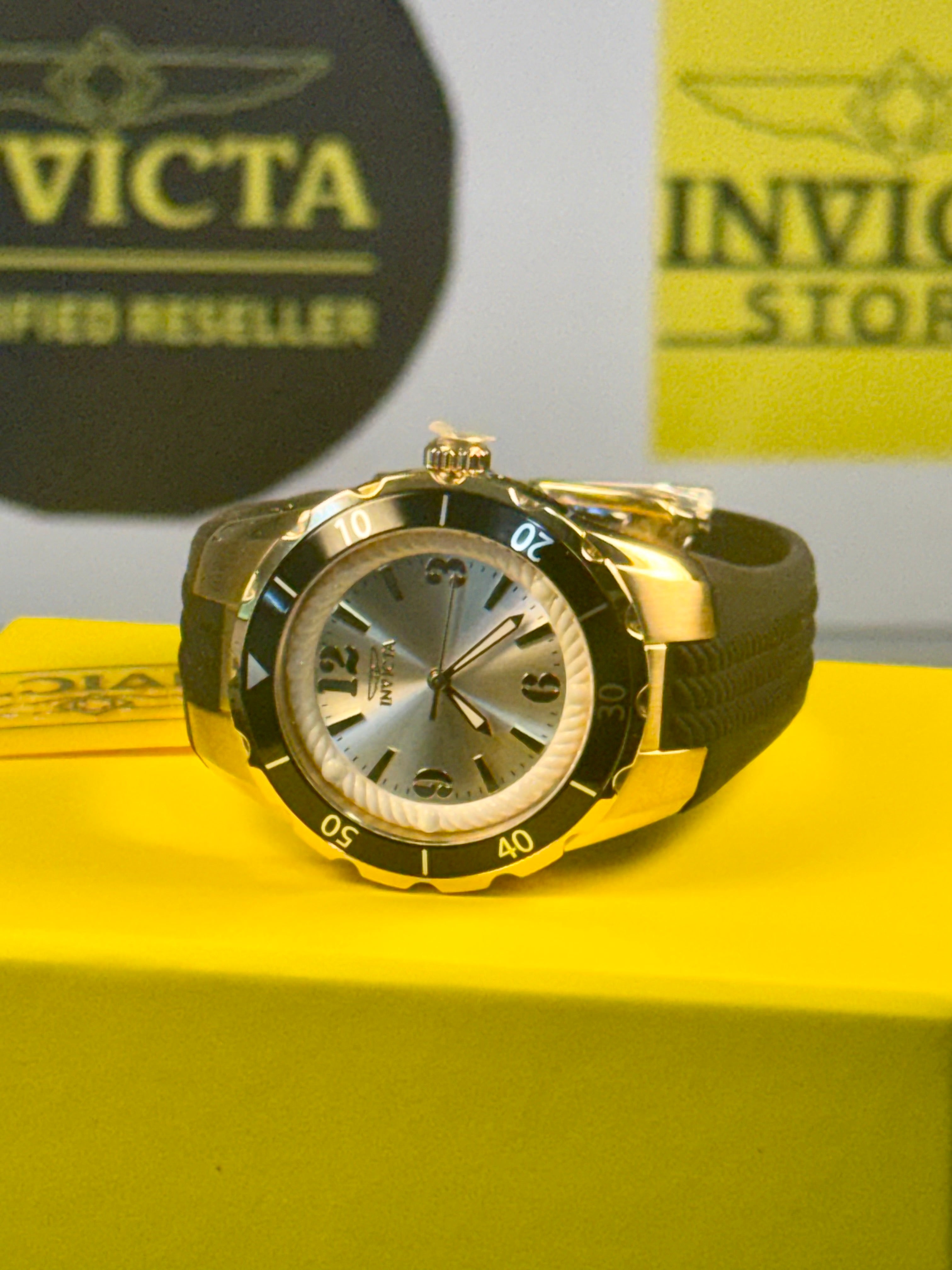 Invicta Ladies Angel  Gold and black watch on a yellow surface with Invicta branding in the background.