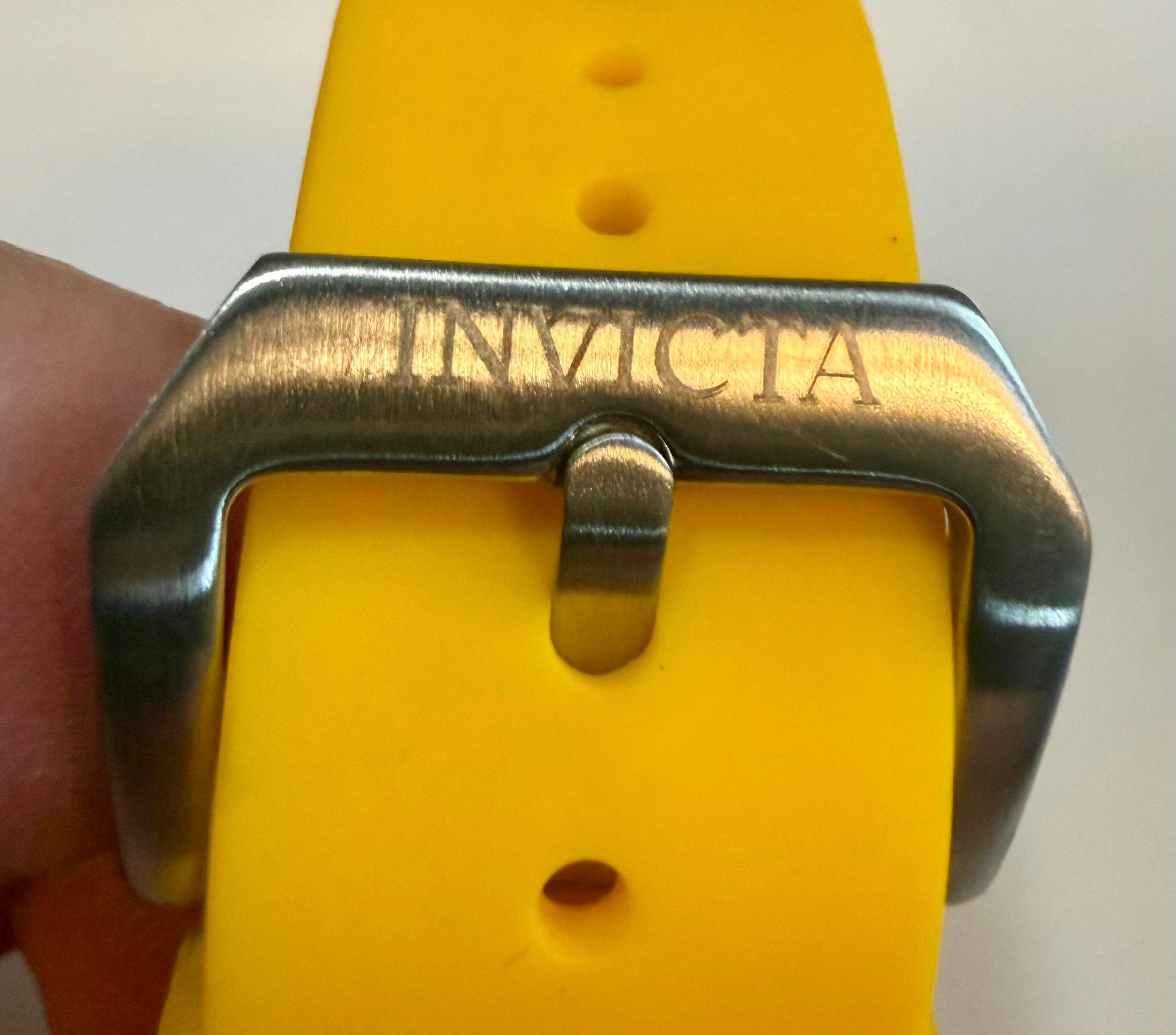 Close-up of a yellow watch strap with a silver buckle featuring 'Invicta' branding.