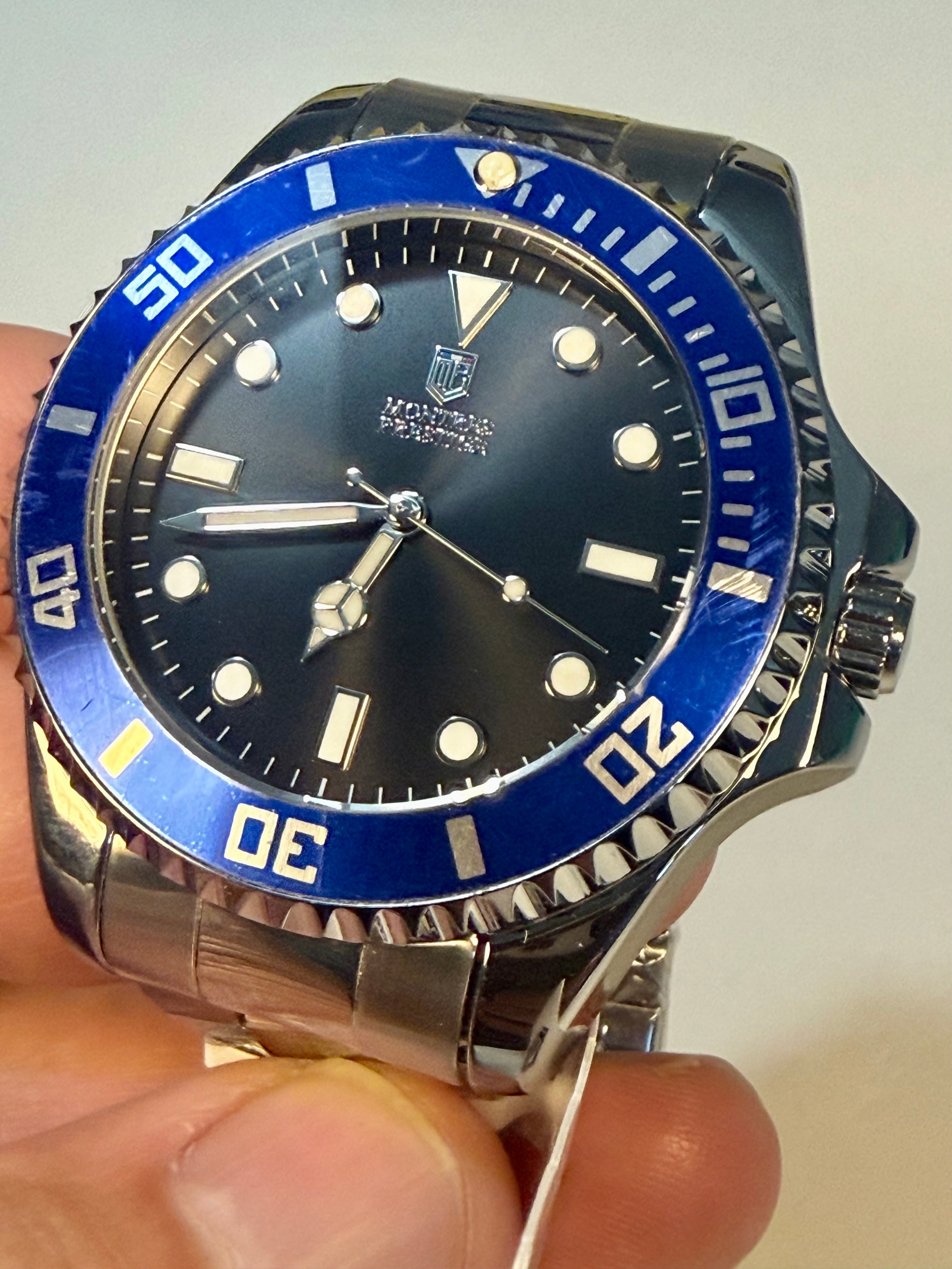 Montres Prestige 42mm Mens Pro Diver Watch with blue bezel and black face held in hand against a neutral background
