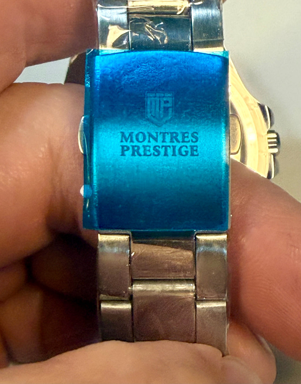Close-up of a Montres Prestige watch with blue face and silver band held in hand.