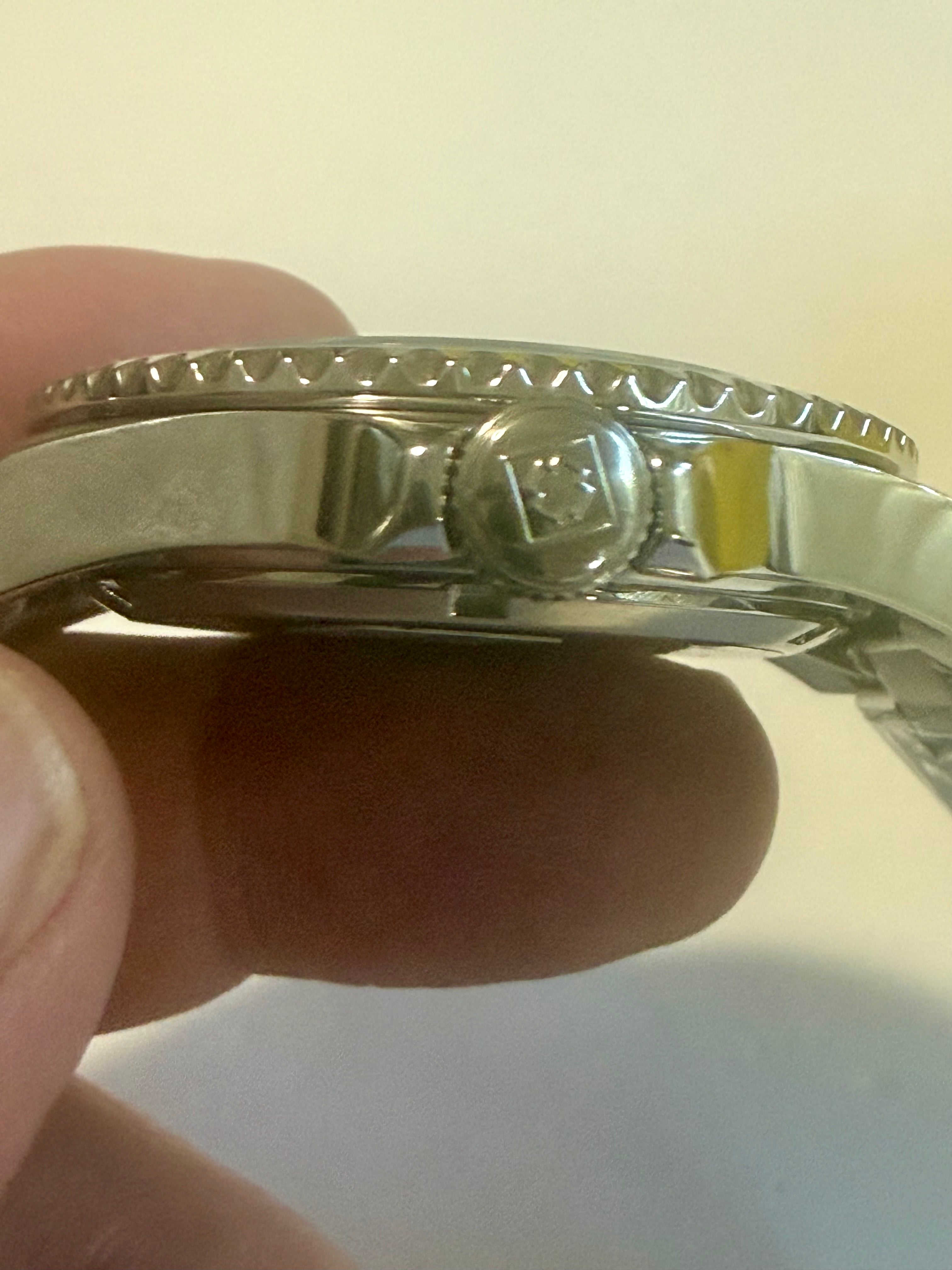 Close-up of a silver watch case held between fingers on a light background