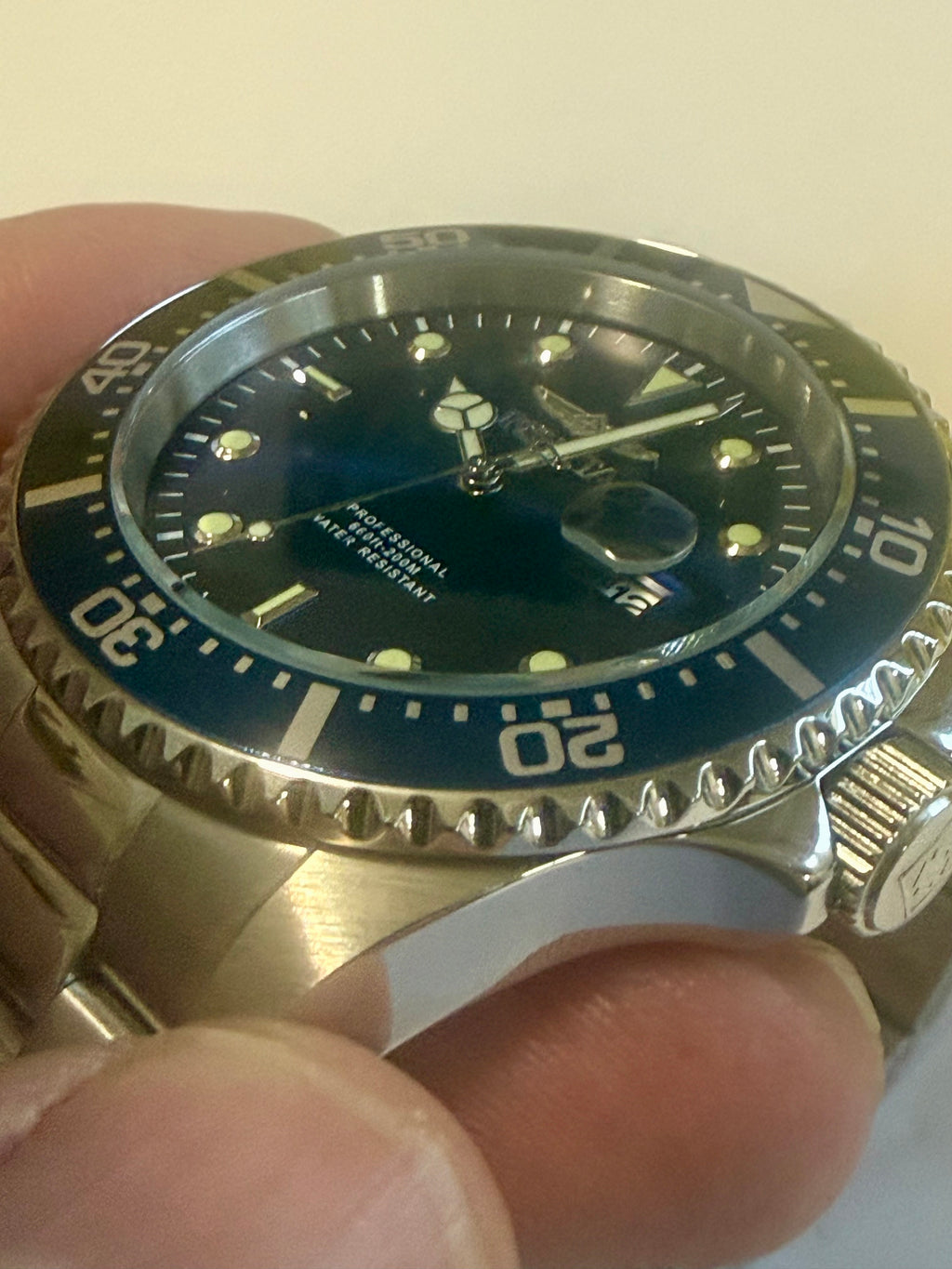 Close-up of a wristwatch with a black dial and blue bezel held by a hand.