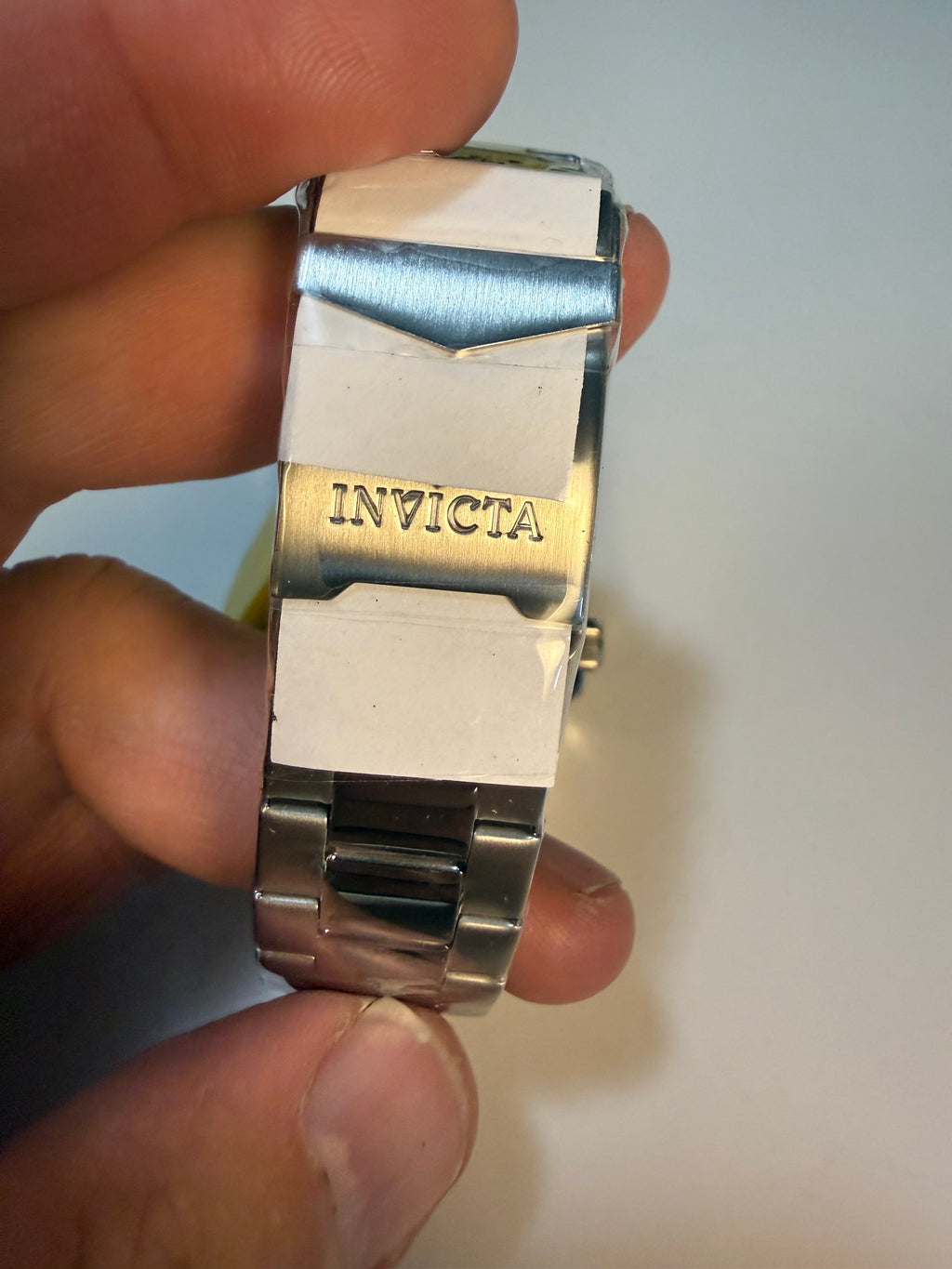 Close-up of a silver Invicta Mens Pro Diver Invicta watch band held between fingers against a neutral background
