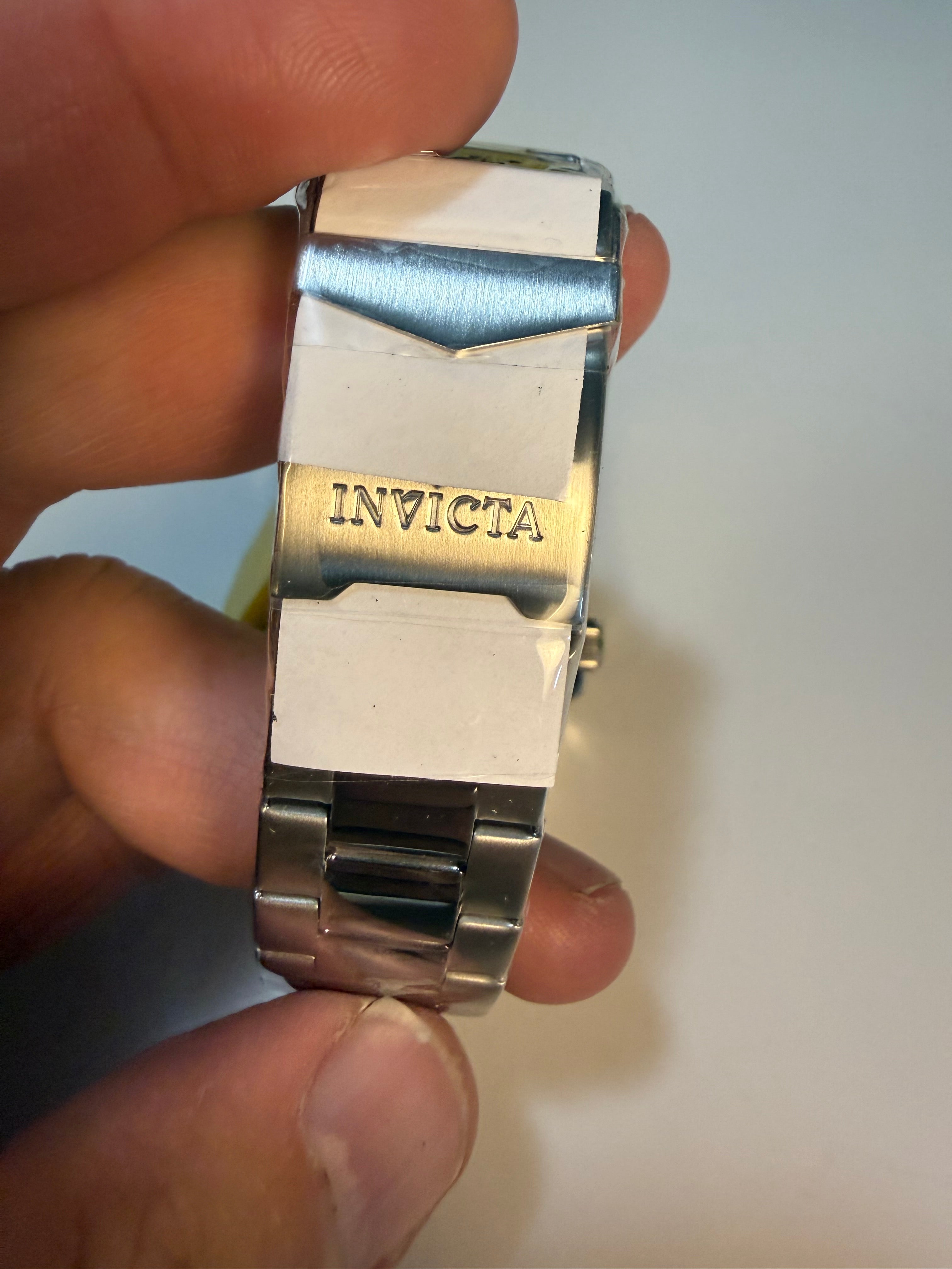 Close-up of a silver Invicta Mens Pro Diver Invicta watch band held between fingers against a neutral background
