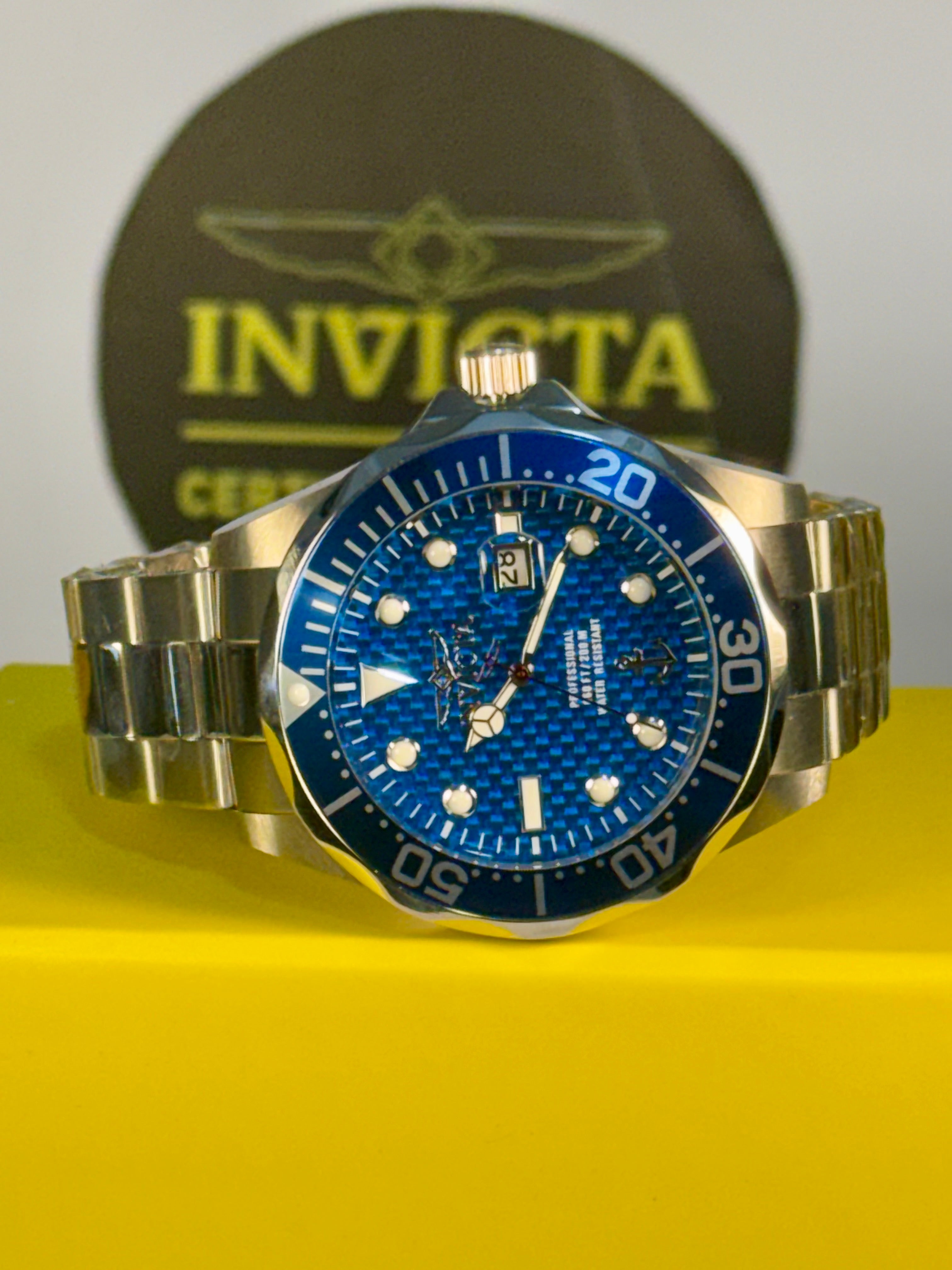 Invicta 47mm Ocean Voyage Silver watch with blue dial on a yellow surface, Invicta logo in the background