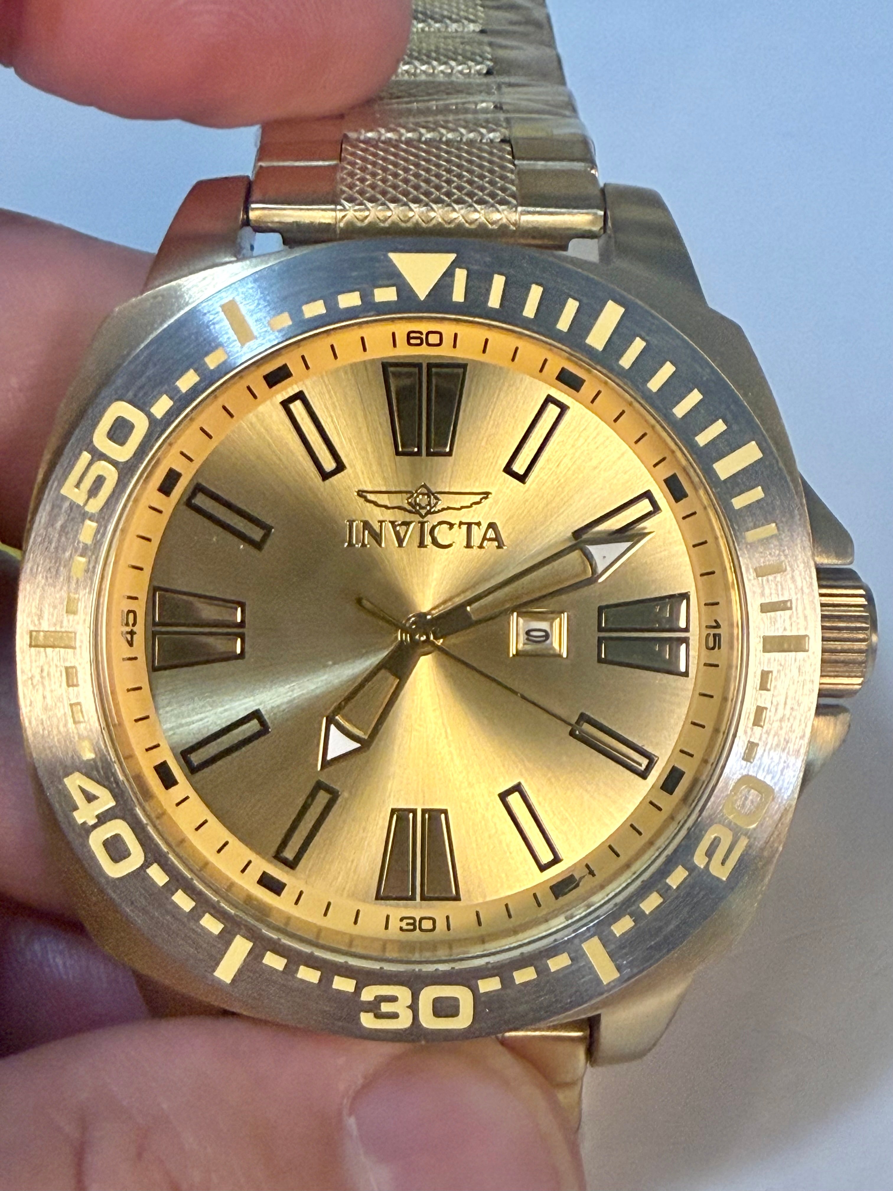 Gold Invicta Speedway 48mm watch held by a hand against a light blue background