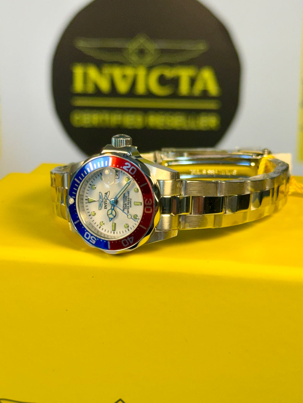 Ladies Pro Diver Silver watch with red and blue accents on a yellow surface, Invicta logo in the background.