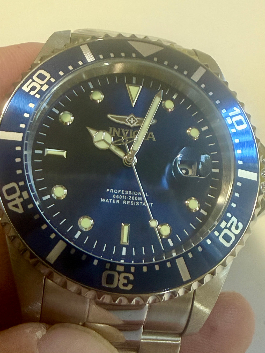 Invicta watch with blue dial and silver bracelet held by a hand.