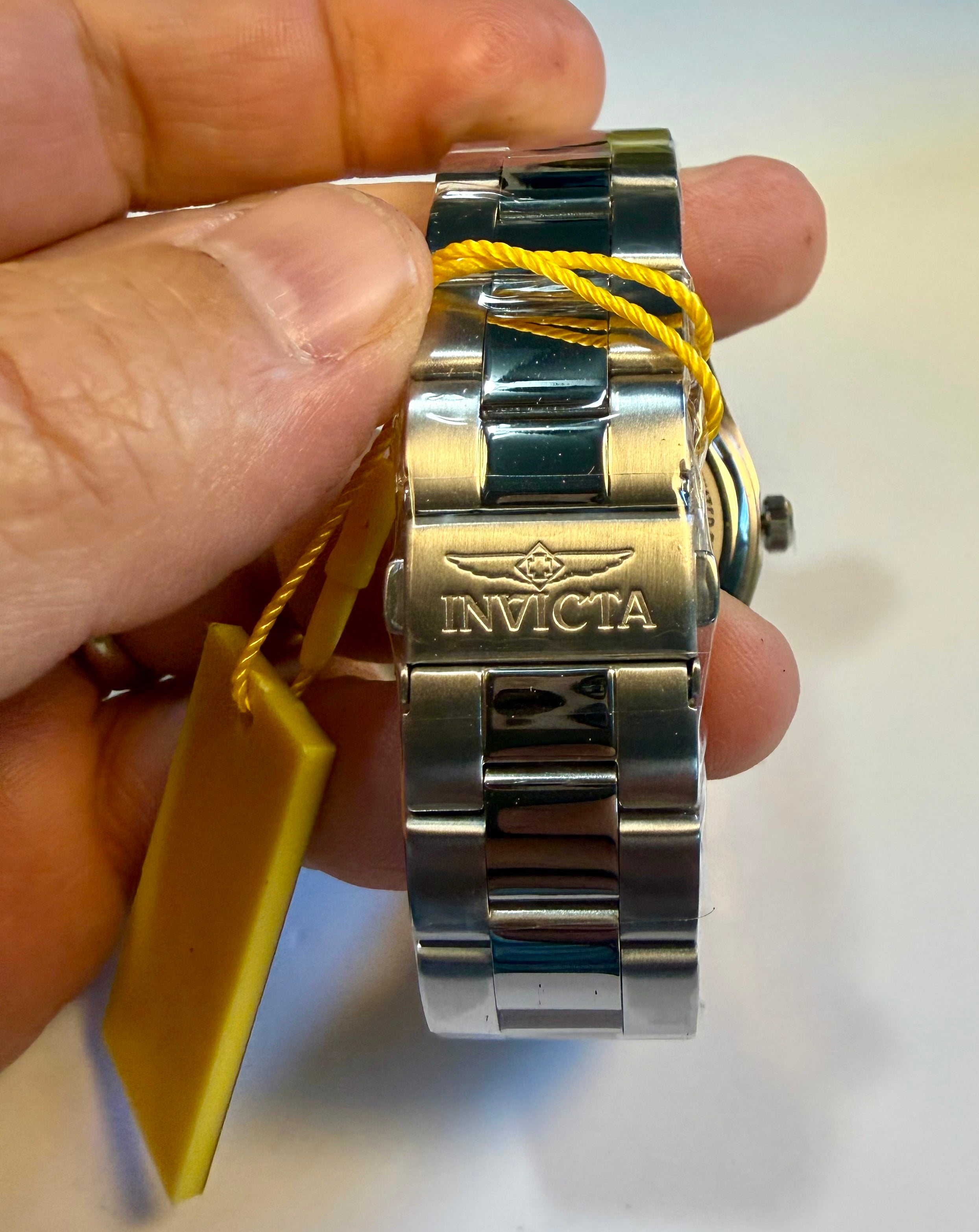 Invicta Specialty Stratford watch with a yellow tag held by a hand on a white background