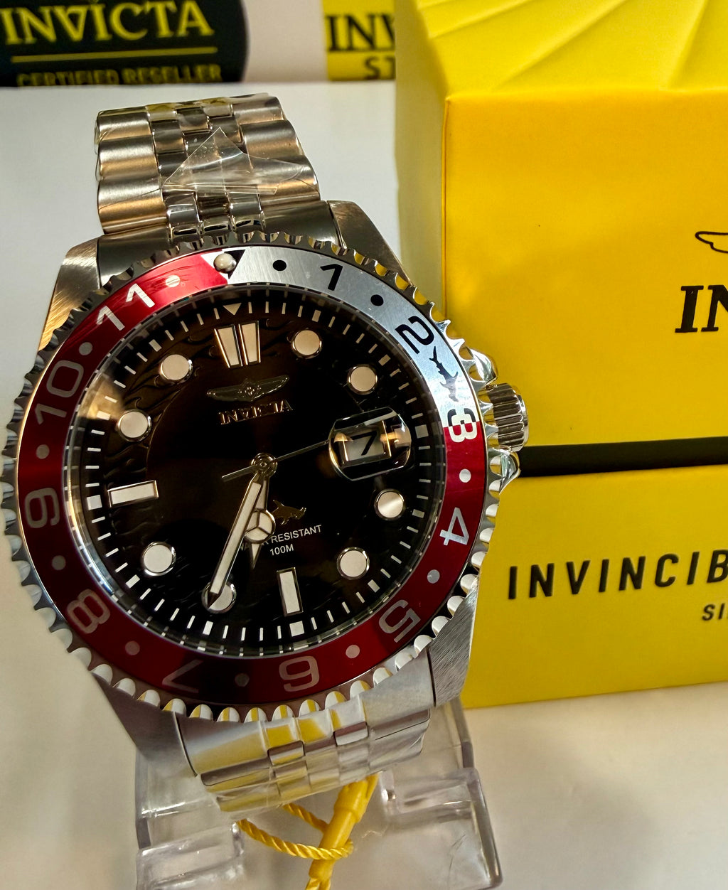 Invicta Mens Pro Diver 43mm Heritage watch with red and black bezel on a stand, yellow box in the background