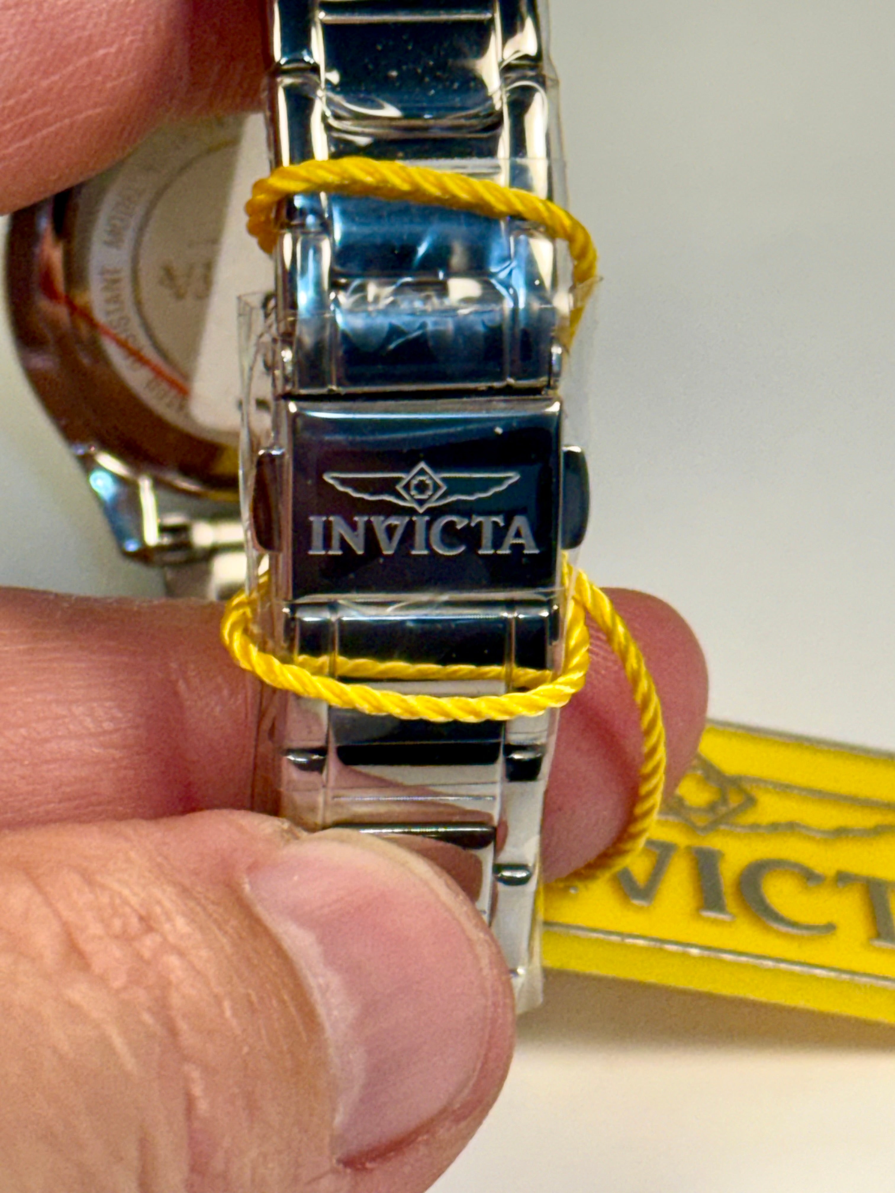 Invicta Ladies Wildflower watch band with yellow string on a hand, Invicta packaging in the background