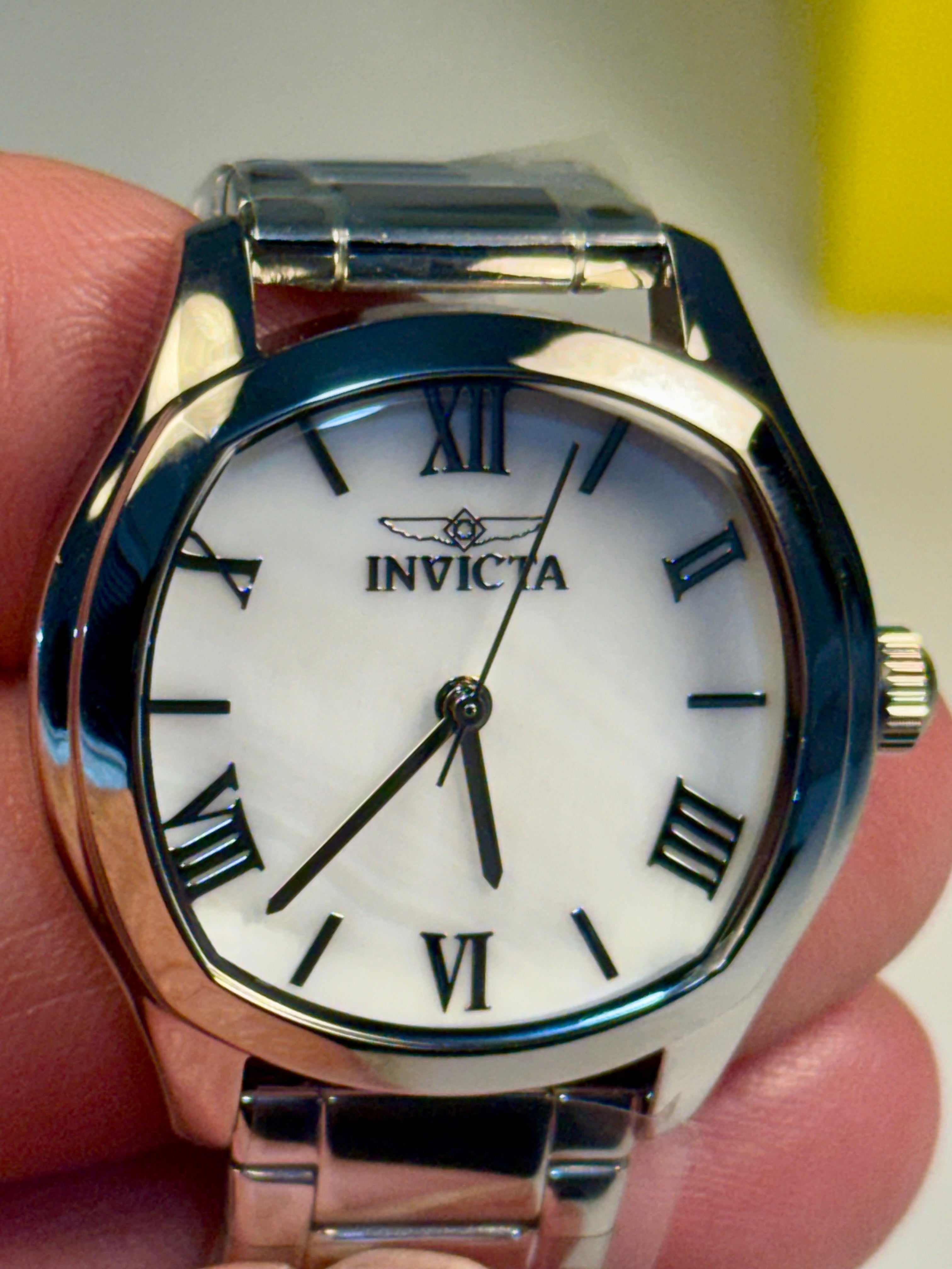 Invicta Ladies Wildflower watch with white face and black Roman numerals held in a hand.