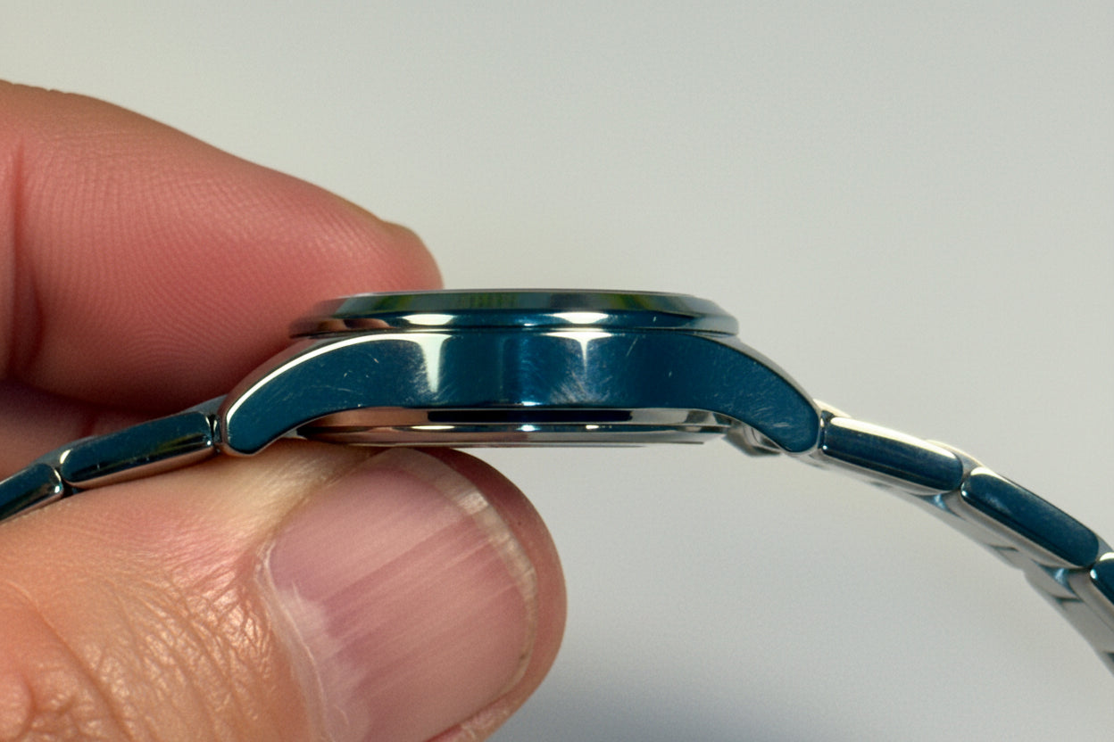 Close-up of a hand holding a blue Invicta Ladies Ocean Voyage watch with a metallic band against a light gray background