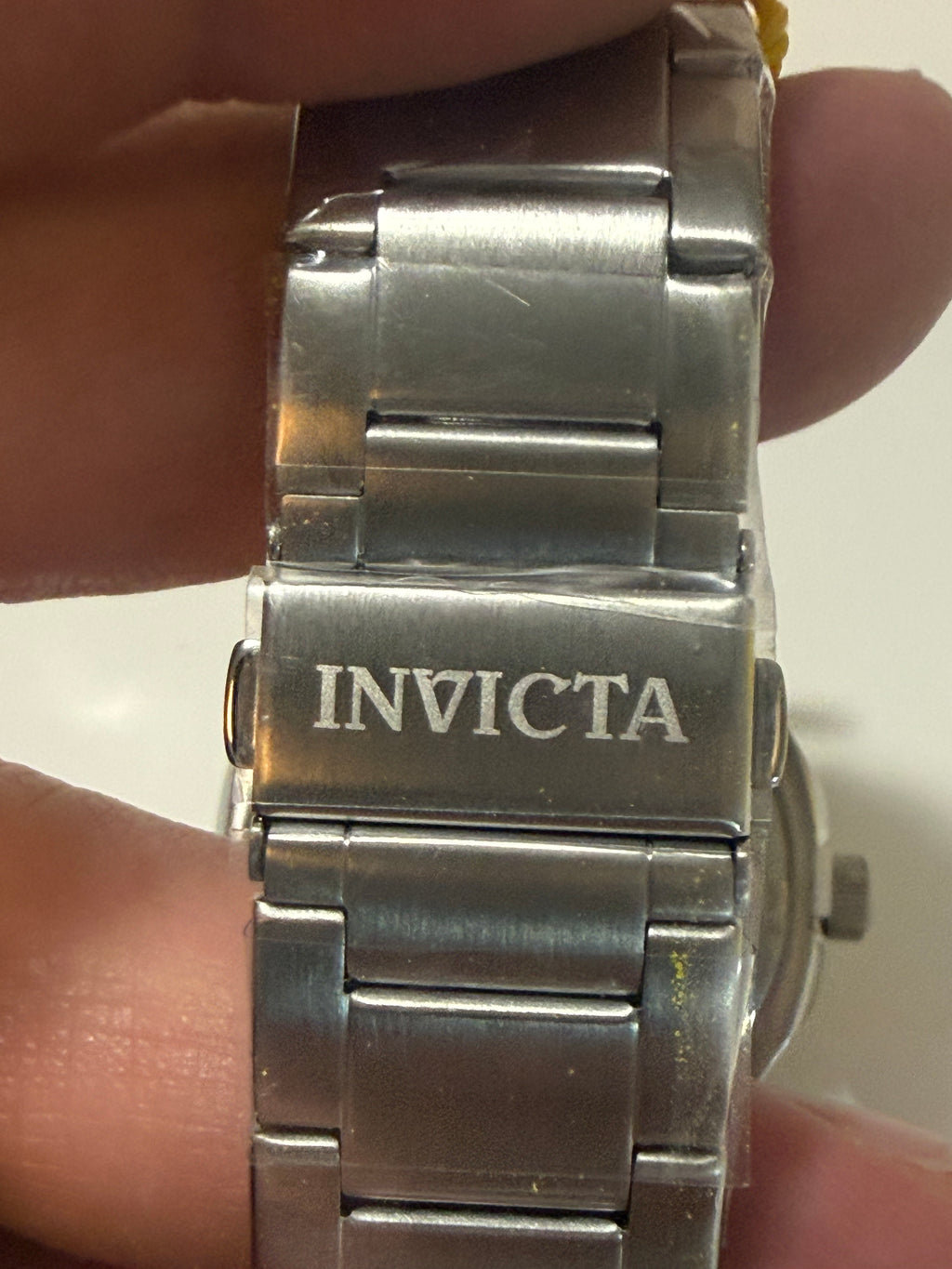 Close-up of a silver Invicta watch band held between fingers.