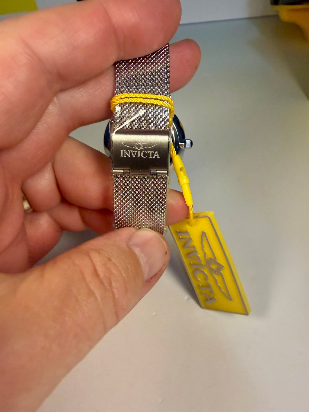 Hand holding a Invicta Angel Starlight   watch with a yellow strap on a light gray surface.