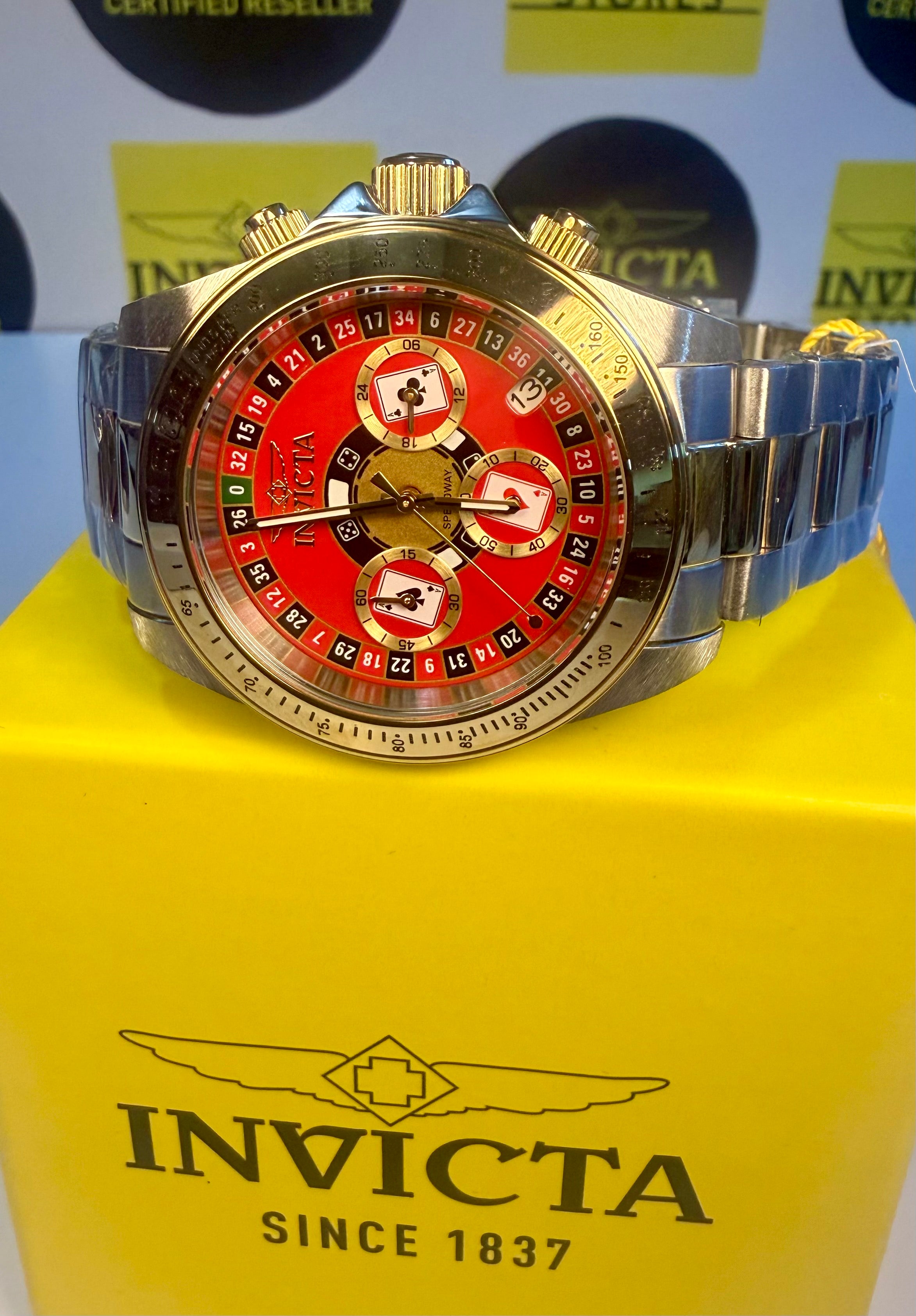 Invicta Speedway Monte Carlo Gold and silver Invicta watch on a yellow box with brand logo