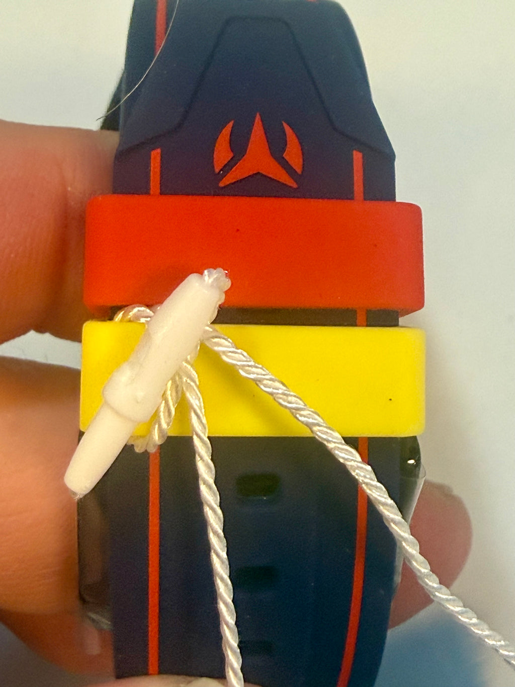 Close-up of a colorful object with a rope, held by a hand against a white background.