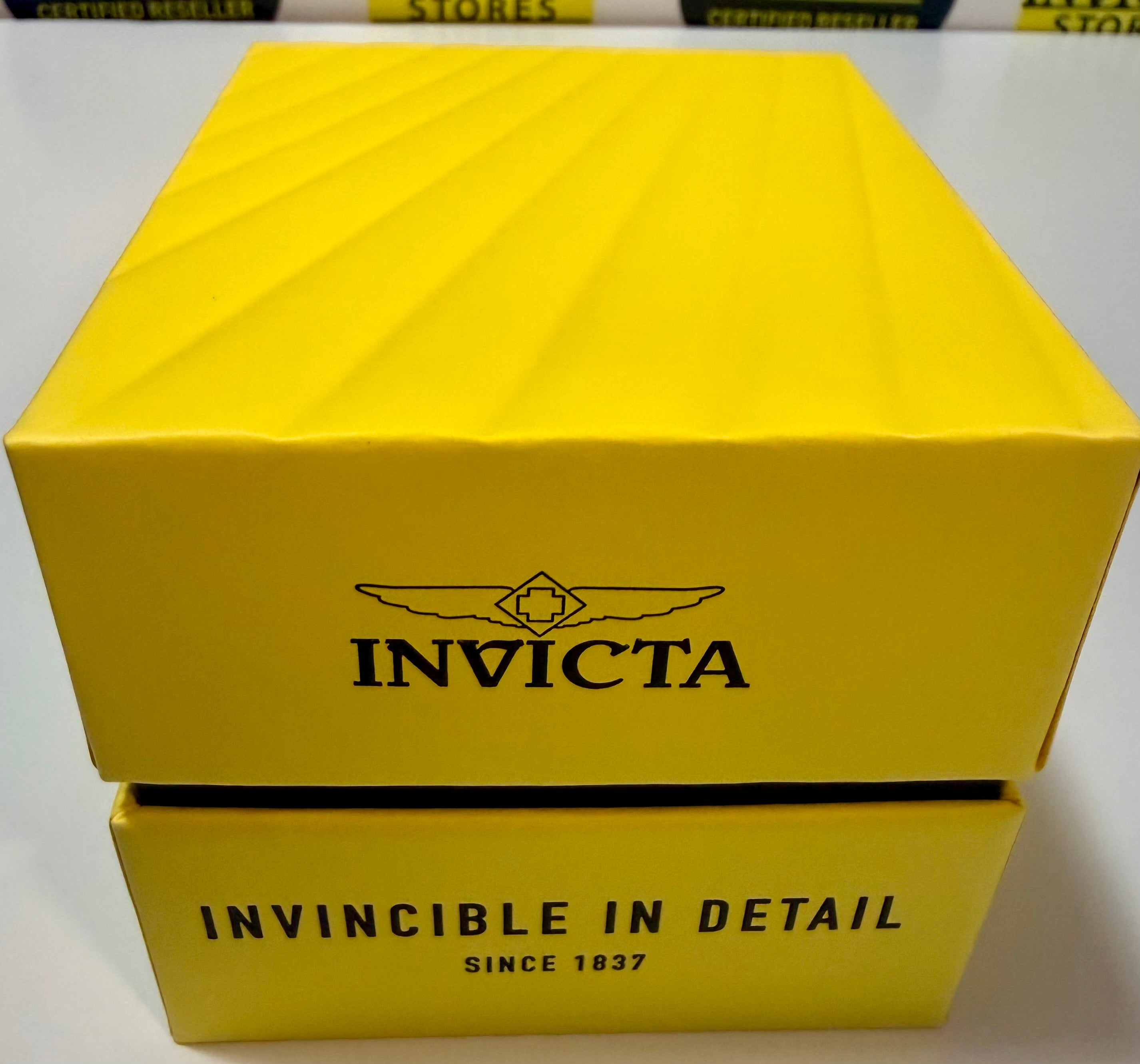 Yellow Invicta watch box with brand logo and tagline on a white background