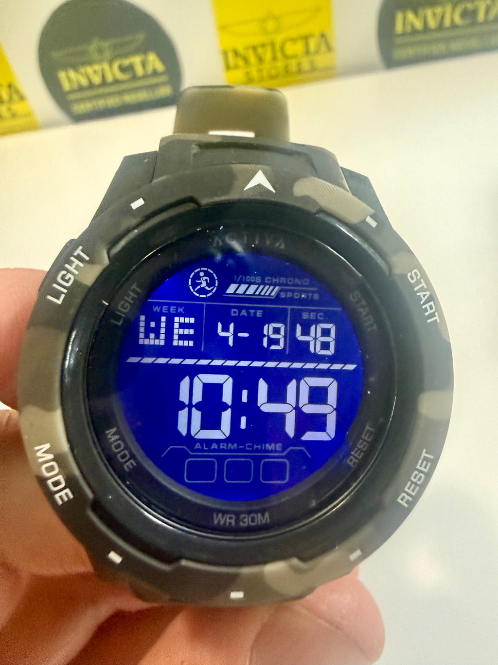 Activa Voyager Camo Digital watch with blue screen held by a hand, Invicta branding in the background