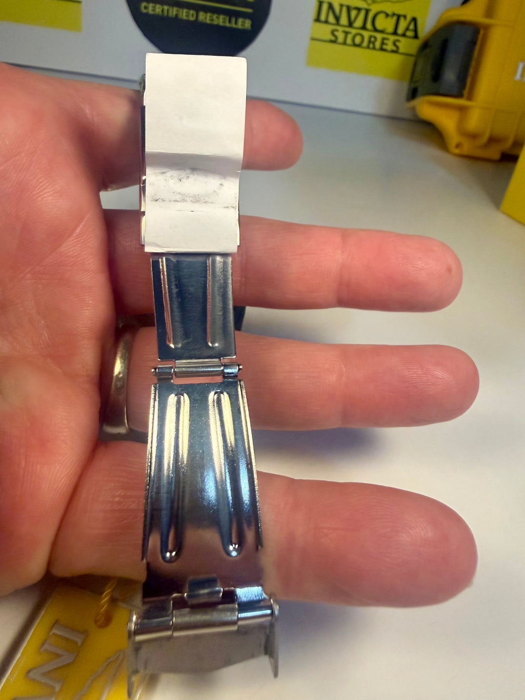 Invicta Specialty Rowan  Metallic watch strap held between fingers with Invicta store sign in background