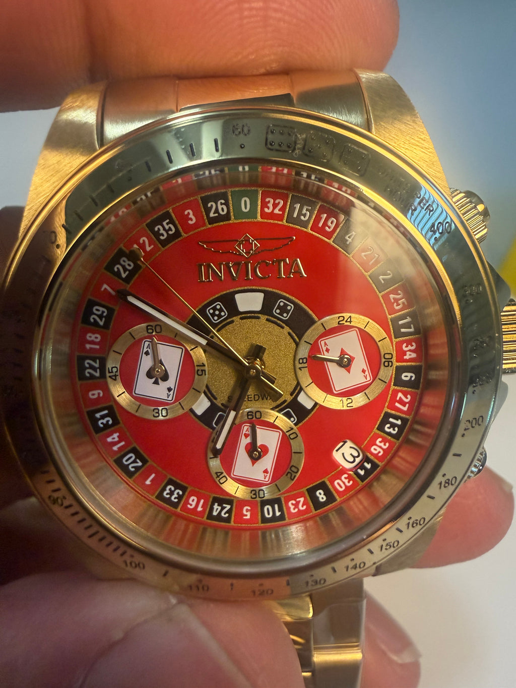 Invicta Speedway Monte Carlo Gold and red Invicta watch held in a hand with a blurred background