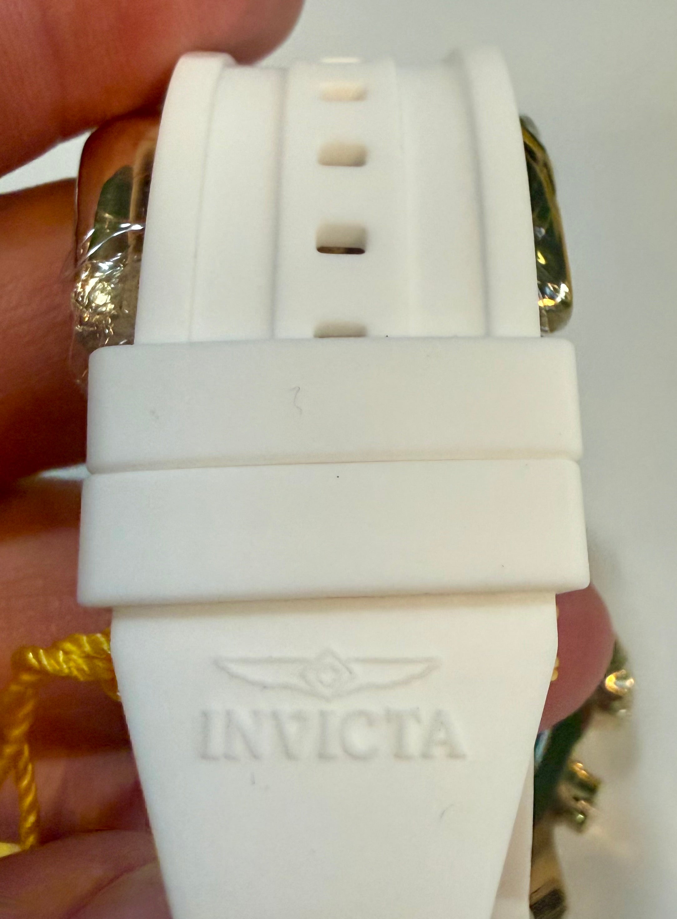 Close-up of a white Invicta watch band held by a hand.
