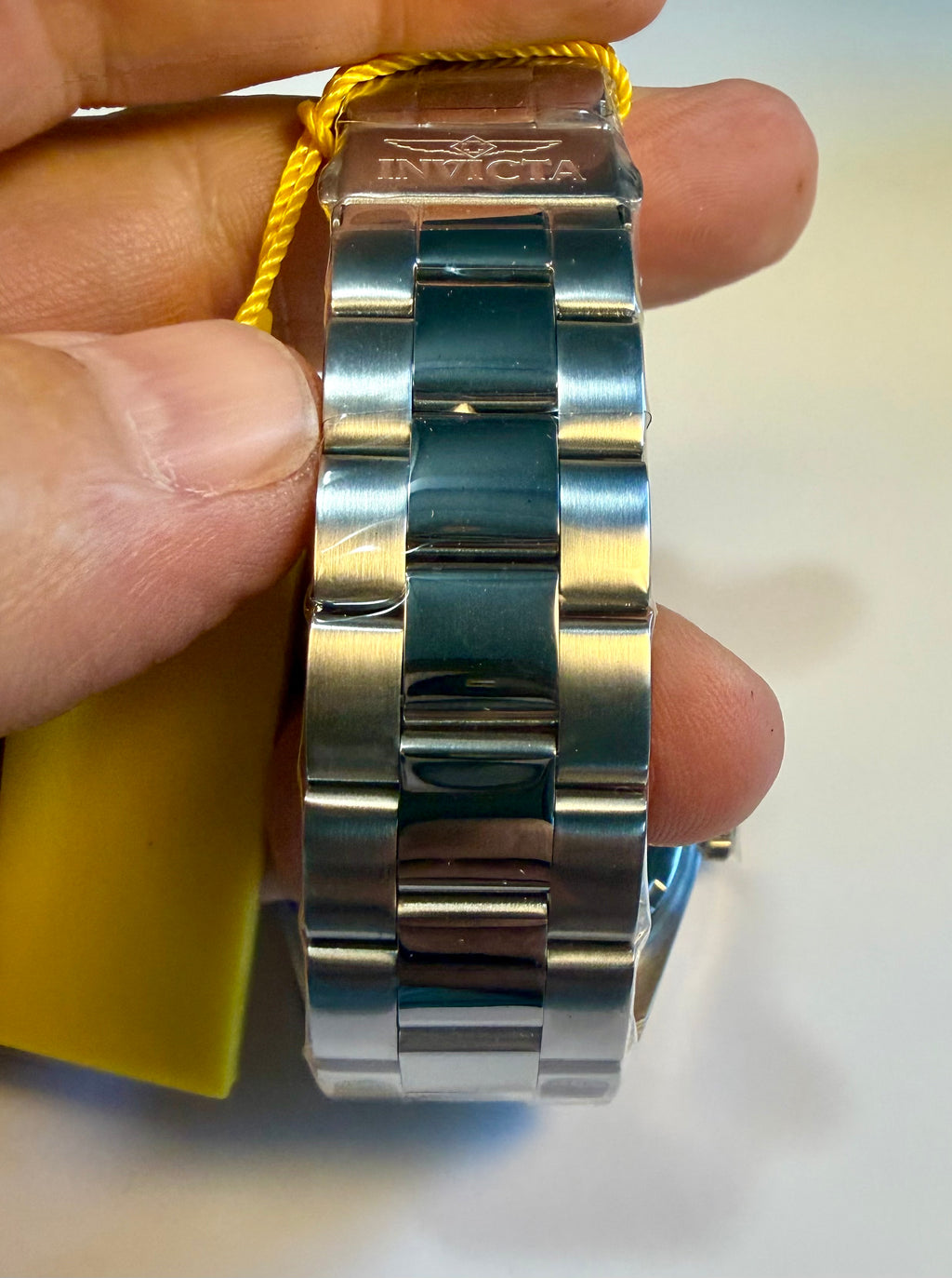Invicta Specialty Stratford watch band with Invicta logo held between fingers on a light background