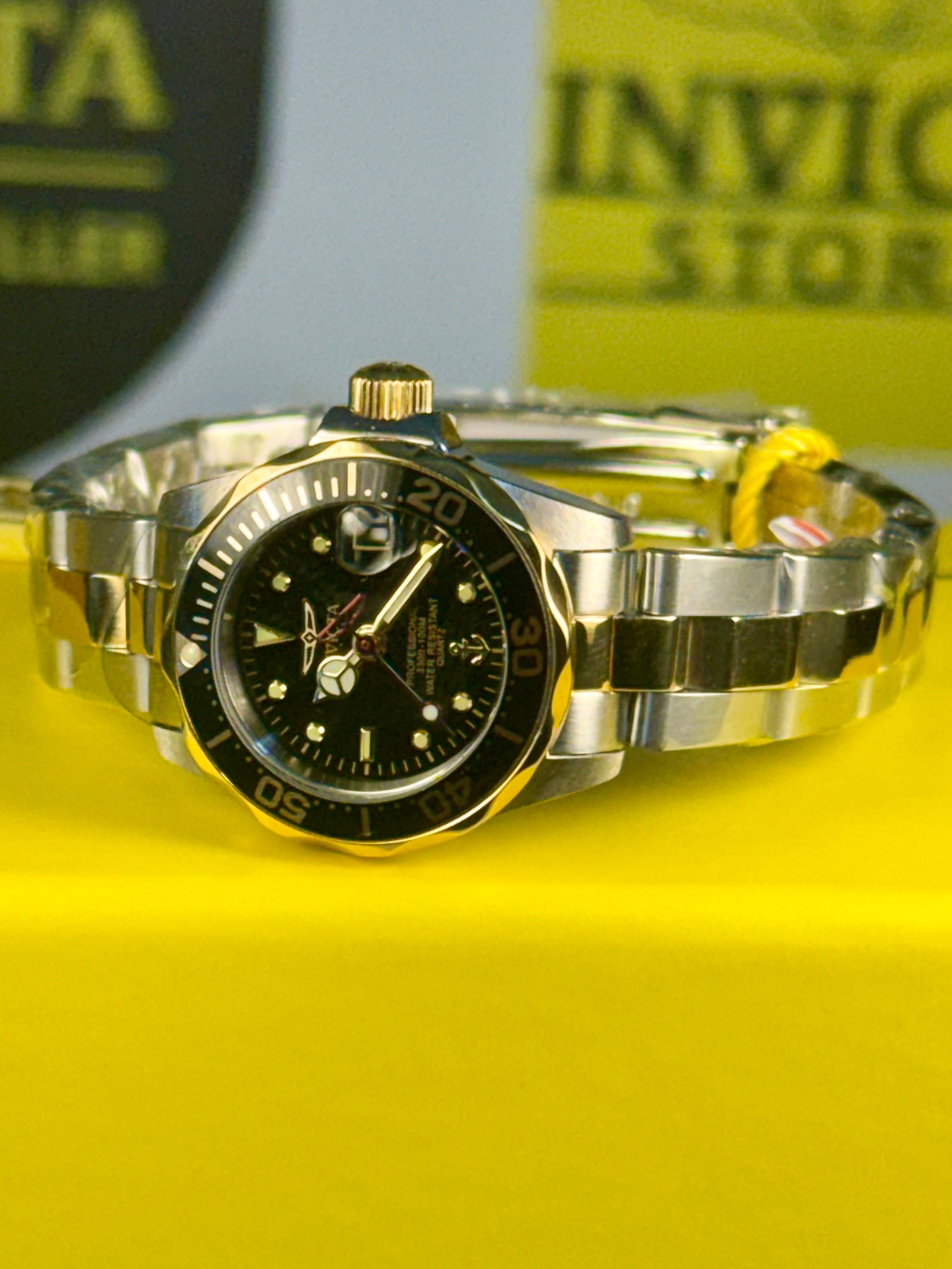 Ladies Invicta Pro Diver 24.5 mm Gold and silver watch with black face on a yellow background