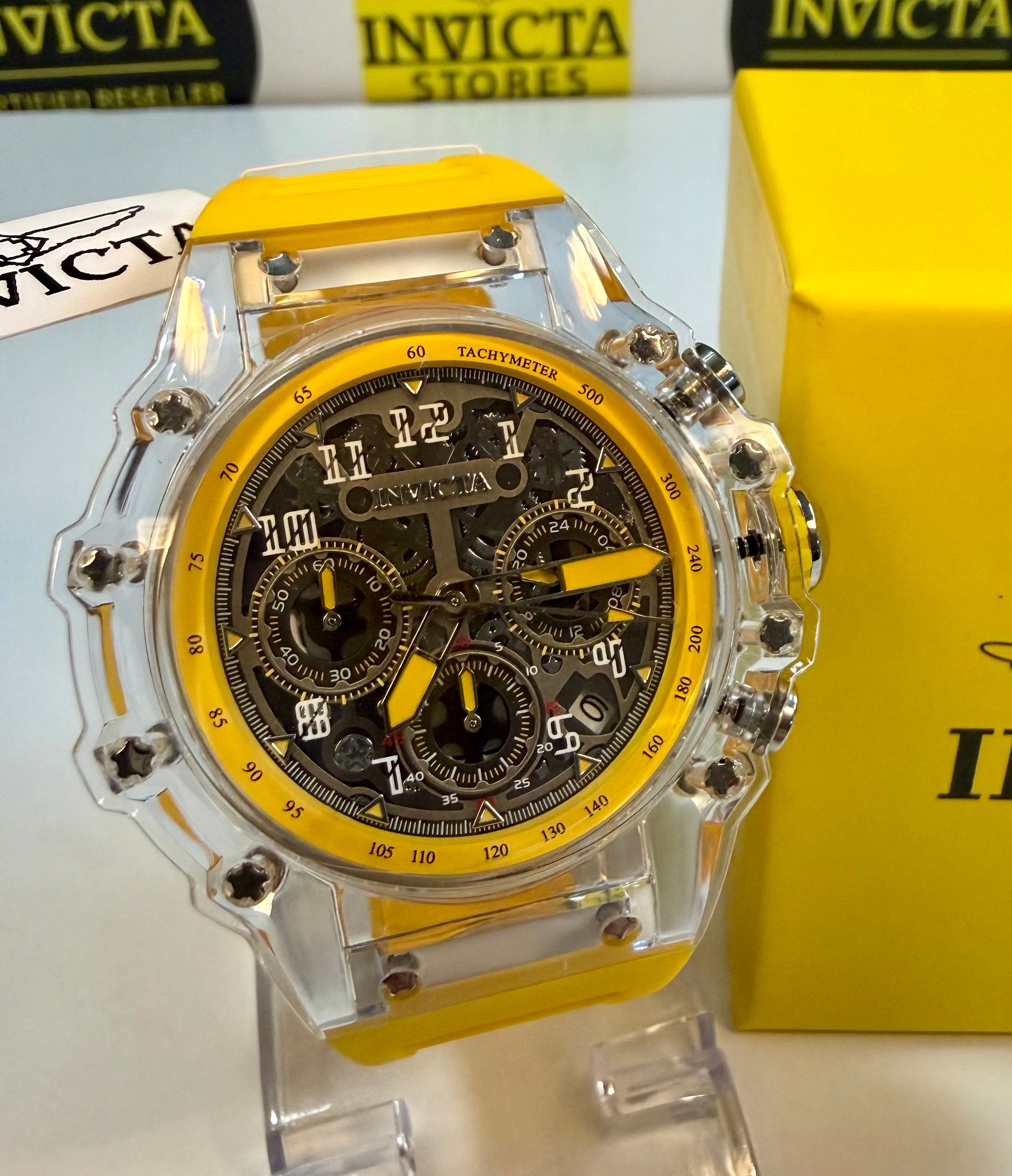 Invicta Racing Vaulthan 44mm watch with yellow accents on a stand, with Invicta box in the background.