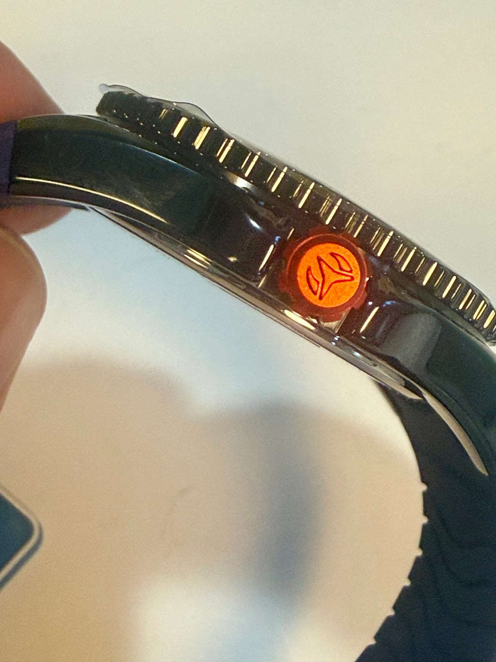 Close-up of a watch with a metallic band and orange button on a blurred background