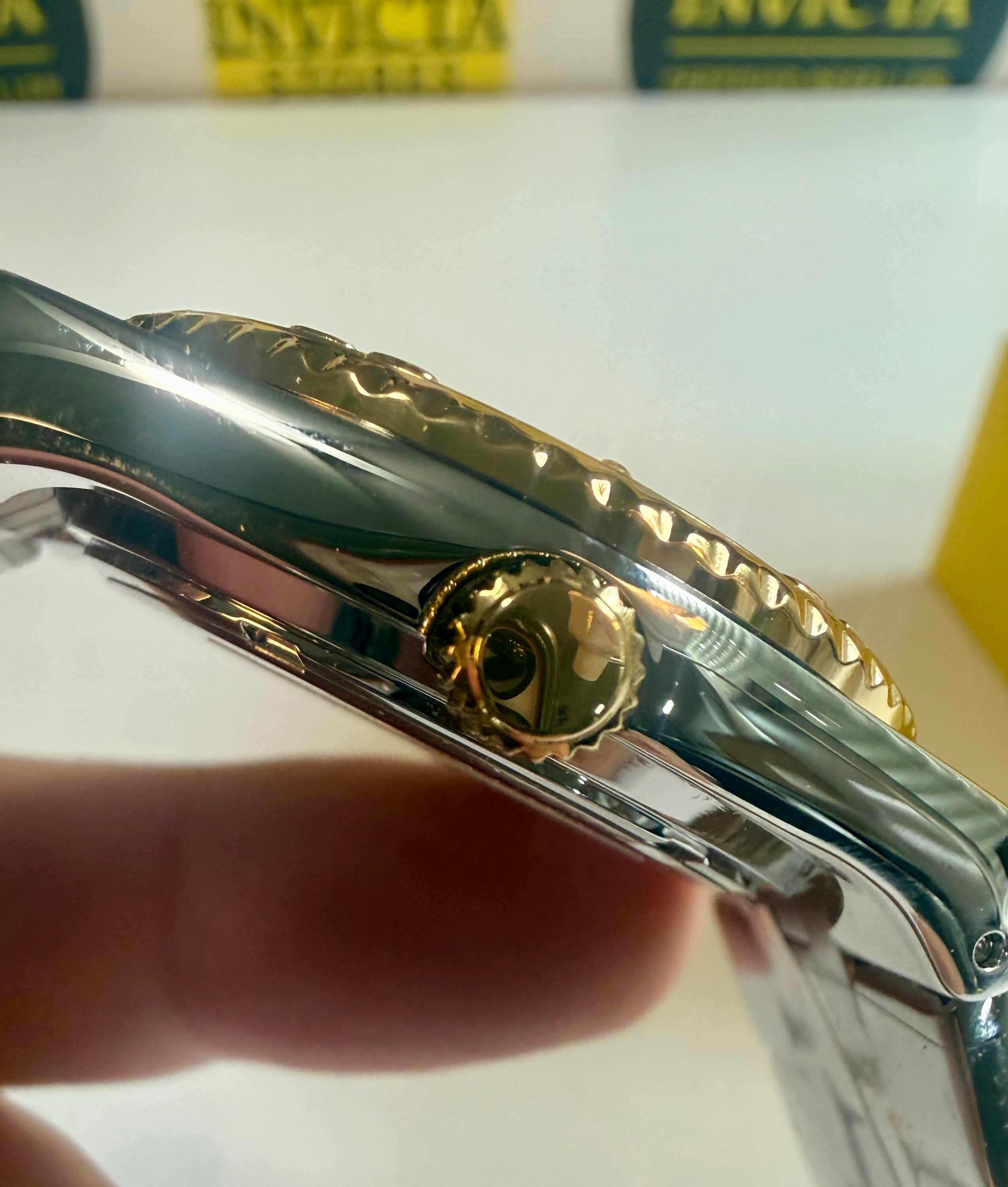 Close-up of a Invicta Ocean Voyage 38mm Pro Diver watch case with gold and silver details, held by a hand.