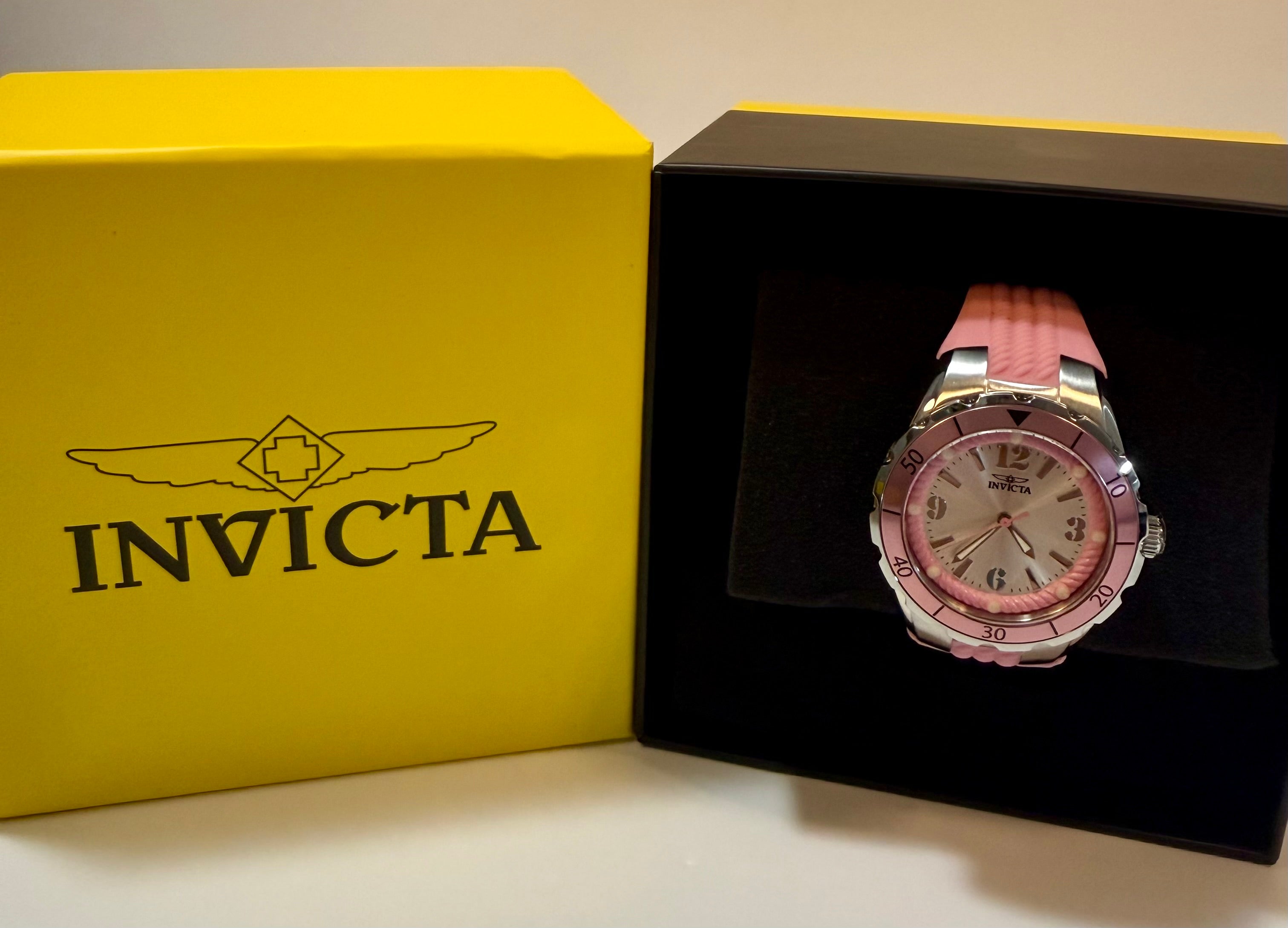 Pink Invicta watch in a black box with a yellow Invicta box in the background.