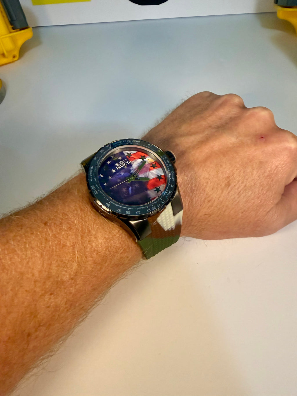 Person wearing a Invicta Aviator Patriotic Camo watch with a colorful face on a plain background