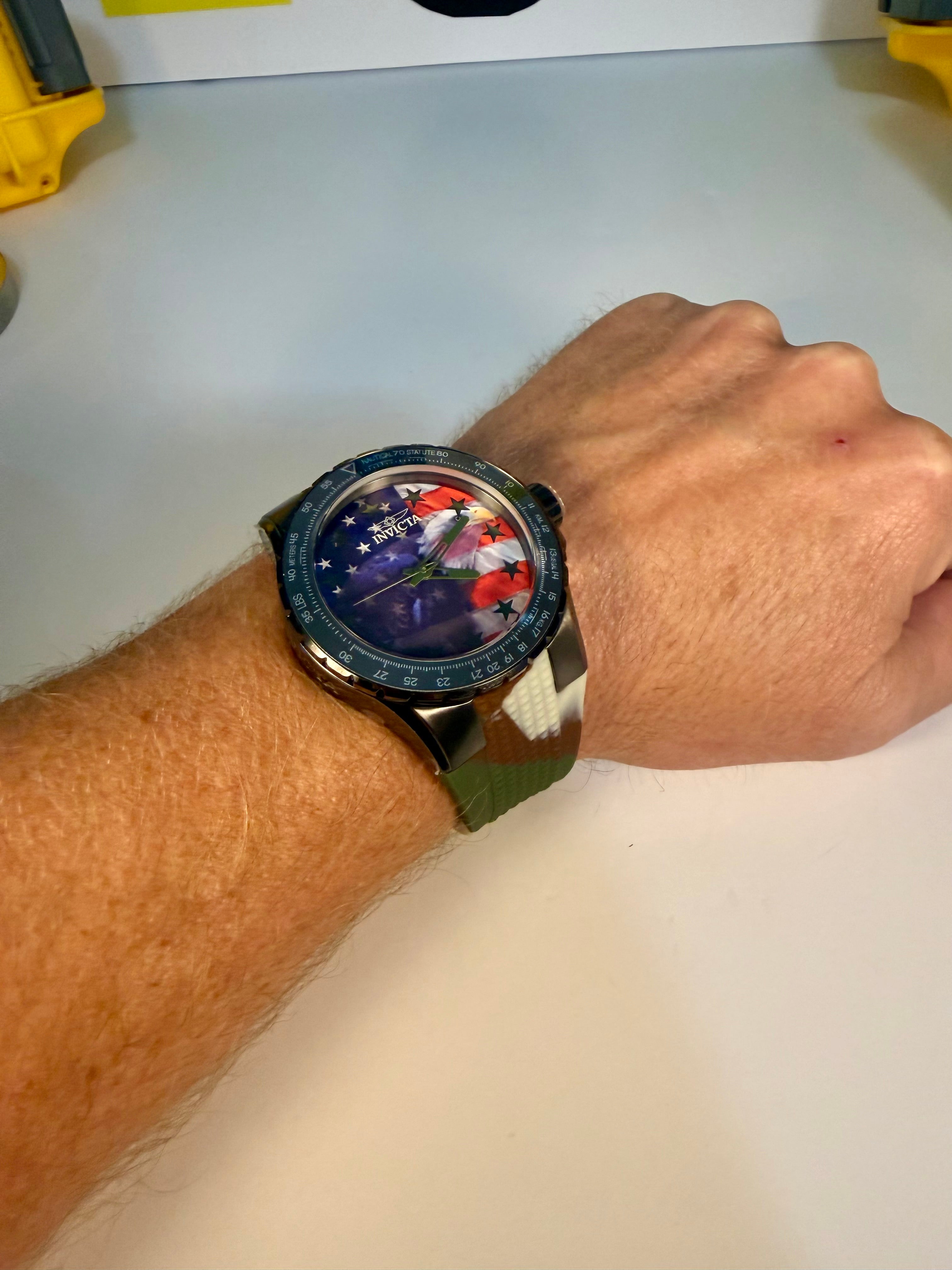 Person wearing a Invicta Aviator Patriotic Camo watch with a colorful face on a plain background