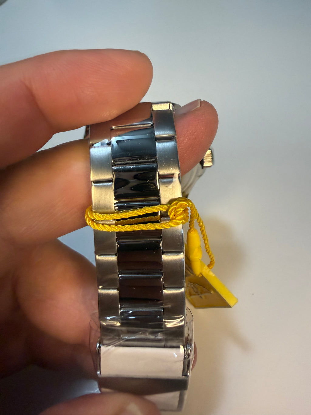 Close-up of a silver Invicta Mens Pro Diver watch band with a yellow strap on a neutral background
