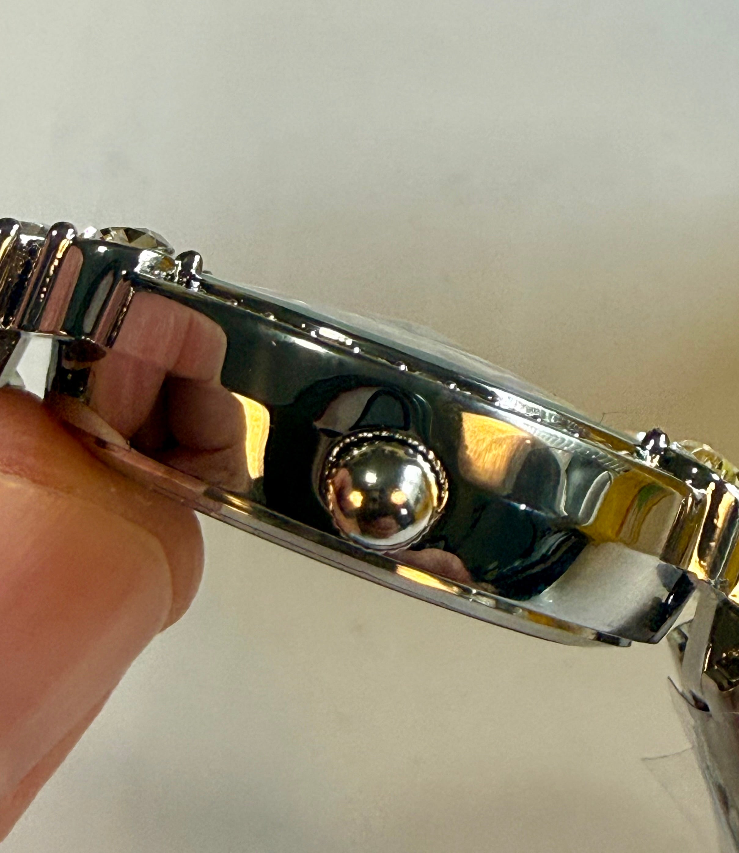 Close-up of a silver Invicta Ladies Wildflower 30mm   with a hand holding it against a white background