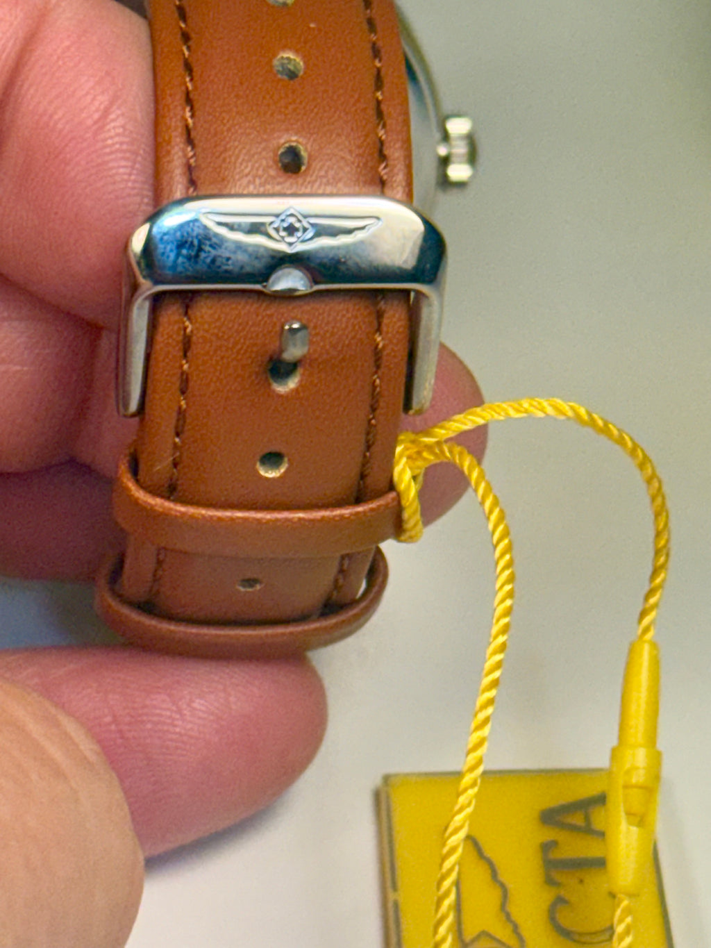 Mens Celestial Blue Sunray Dial Brown leather watch strap with silver buckle held by a hand, with a yellow tag in the background.