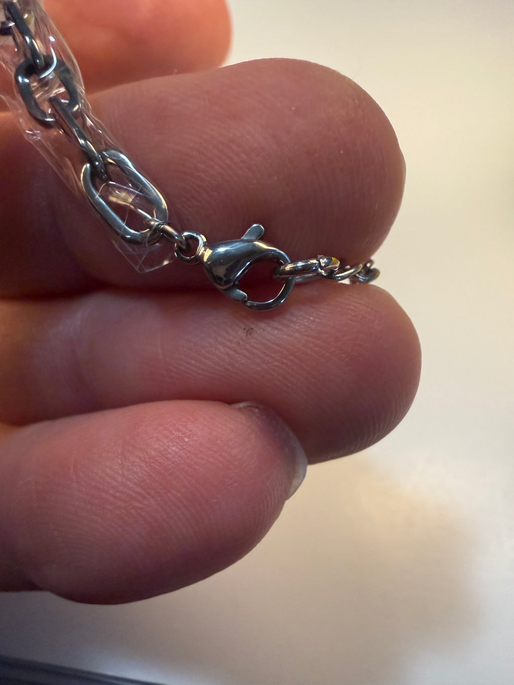 Close-up of a silver bracelet clasp held between fingers against a neutral background