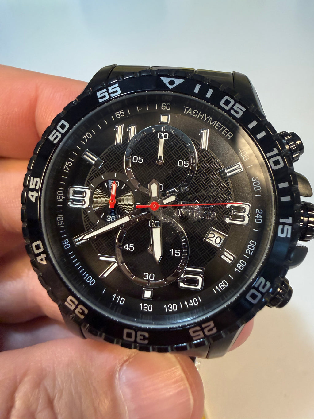Invicta Mens Specialty Fortitude Black chronograph watch held in a hand with a light background